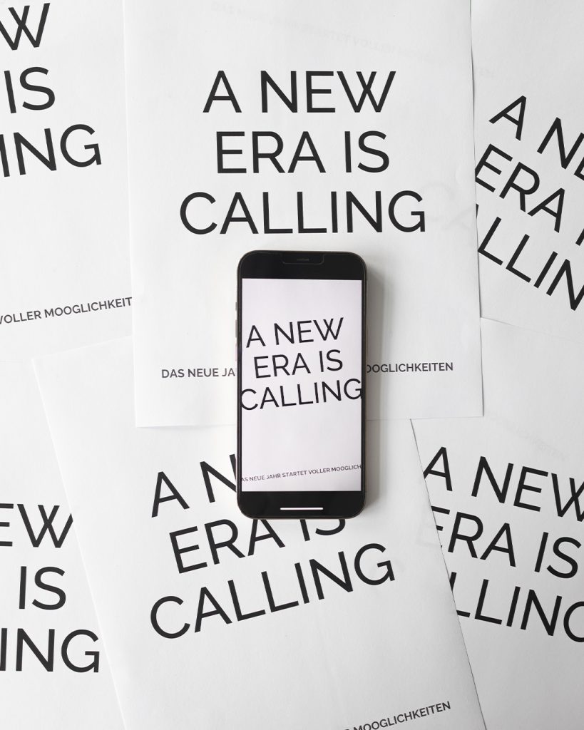 Ein Handy liegt auf mehreren Blättern Papier, beschrieben mit dem Satz "A New Era is Calling".